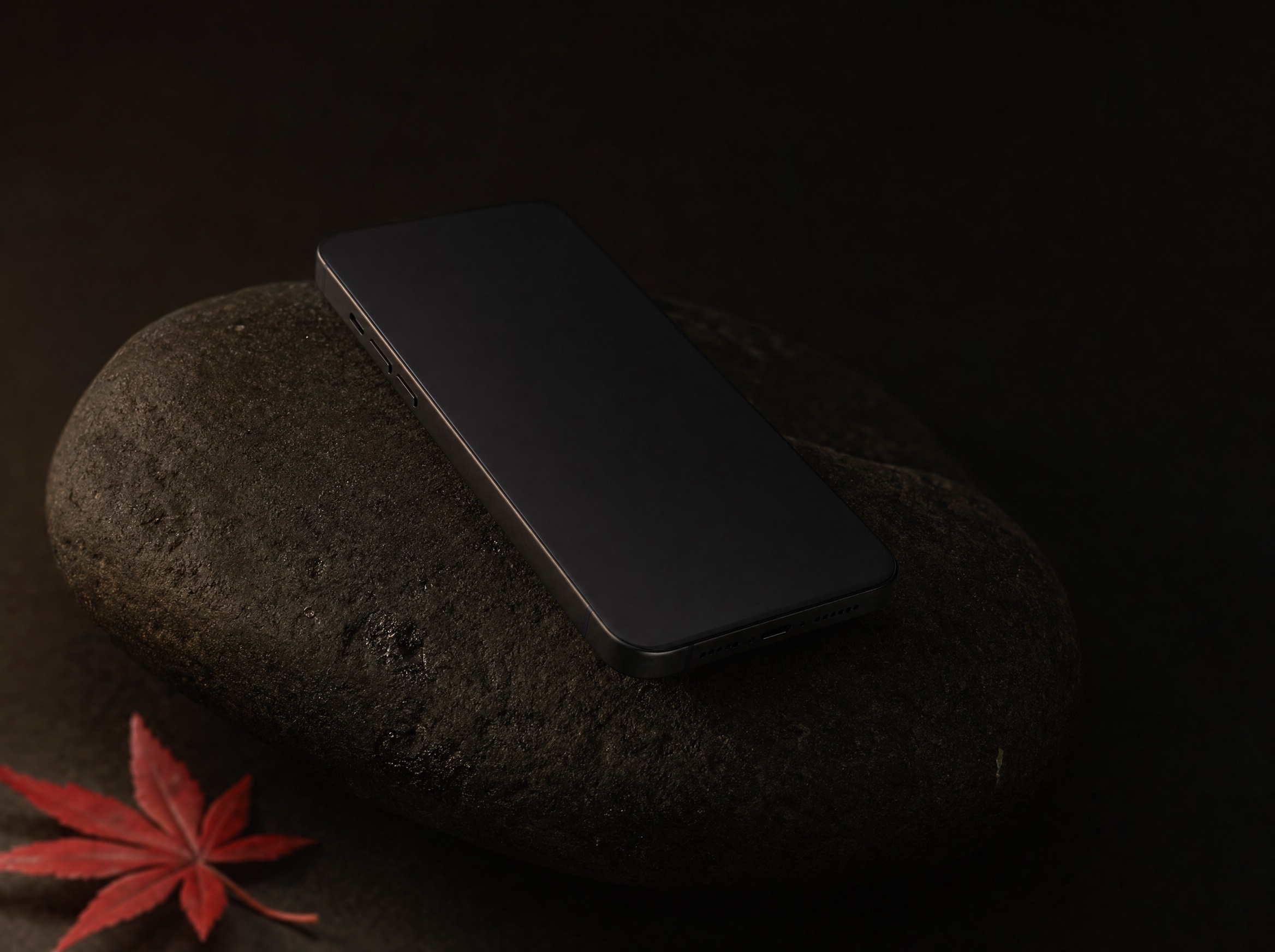 The ISHI phone resting on a dark river stone beside a red maple leaf