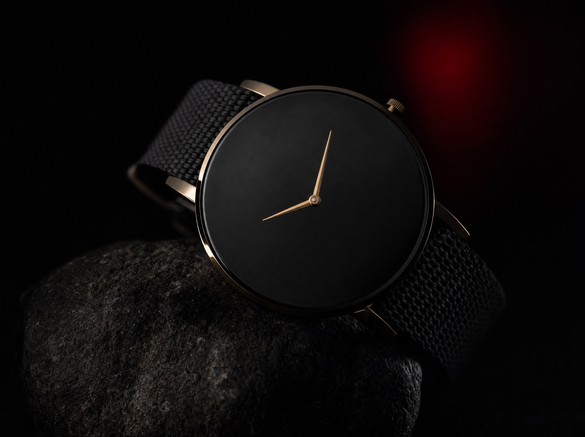 The TOKI watch with a blank obsidian dial and two gold hands, draped over dark stone
